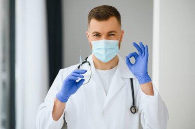 Mavi eldivenli bir doktor elinde aşıyla bir şişe tutuyor. Yakın çekim. Tıp ve sağlık hizmetleri kavramı