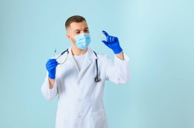 Tıbbi maskeli genç bir doktor ve steteskobu olan beyaz önlüklü mavi şırıngayı tutan.
