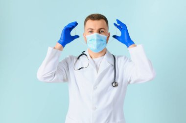Tıbbi eldivenli bir adam mavi arka planda koruyucu yüz maskesi takıyor.