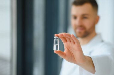 Mavi eldivenli bir doktor elinde aşıyla bir şişe tutuyor. Yakın çekim. Tıp ve sağlık hizmetleri kavramı