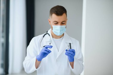 Mavi eldivenli bir doktor elinde aşıyla bir şişe tutuyor. Yakın çekim. Tıp ve sağlık hizmetleri kavramı