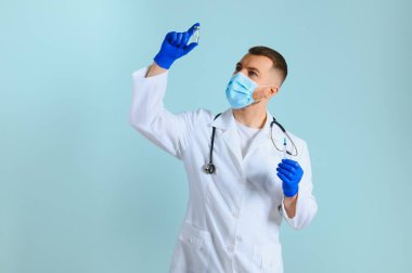 Koronavirüse karşı aşı. COVID-19 aşıları test ediliyor. Tıbbi maskeli bir erkek doktor mavi arka planda COVID-19 aşısı olan bir şırınga dolduruyor. Doktorun elleri şırıngayı yakın çekimde tutuyor..
