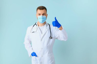 Tıbbi maske takan genç bir erkek doktor ve boynunda steteskop var. Mavi arka planda izole edilmiş.