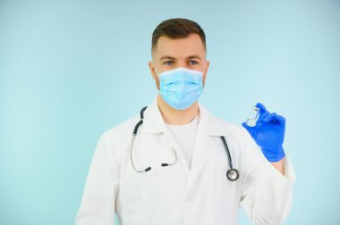 Koronavirüse karşı aşı. COVID-19 aşıları test ediliyor. Tıbbi maskeli bir erkek doktor mavi arka planda COVID-19 aşısı olan bir şırınga dolduruyor. Doktorun elleri şırıngayı yakın çekimde tutuyor..