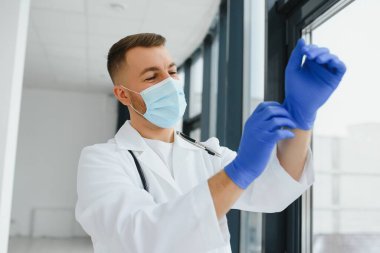 Beyaz üniformalı, gözlüklü, boynunda steteskop olan ve hasta muayenesinden önce lastik eldiven takan beyaz erkek doktor..