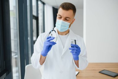 Mavi eldivenli bir doktor elinde aşıyla bir şişe tutuyor. Yakın çekim. Tıp ve sağlık hizmetleri kavramı