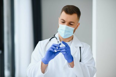 Mavi eldivenli bir doktor elinde aşıyla bir şişe tutuyor. Yakın çekim. Tıp ve sağlık hizmetleri kavramı