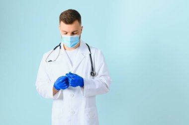 Koronavirüse karşı aşı. COVID-19 aşıları test ediliyor. Tıbbi maskeli bir erkek doktor mavi arka planda COVID-19 aşısı olan bir şırınga dolduruyor. Doktorun elleri şırıngayı yakın çekimde tutuyor..
