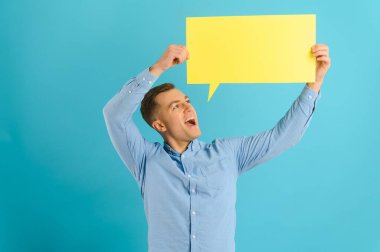 Elinde boş konuşma balonu işareti tutan yakışıklı adam açık mavi stüdyo arkaplanında fotokopi alanı ile izole edilmiş.