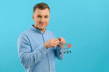 Mavi arka planda küçük alışveriş sepetleri tutan gülümseyen adamın portresi. Satışları artırma kavramı.