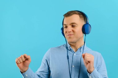 Renkli arka planda poz veren yakışıklı bir genç. Genç adam kulaklıkla müzik dinliyor..