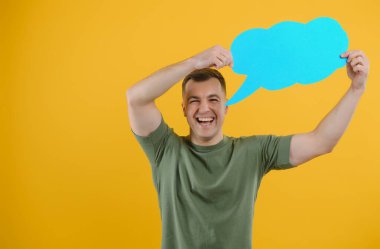 Neşeli genç erkek boş bir konuşma baloncuğu tutuyor ve parlak sarı arka plana karşı boş bir alan yaratıyor.