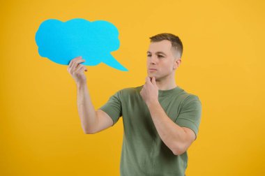 Neşeli genç erkek boş bir konuşma baloncuğu tutuyor ve parlak sarı arka plana karşı boş bir alan yaratıyor.