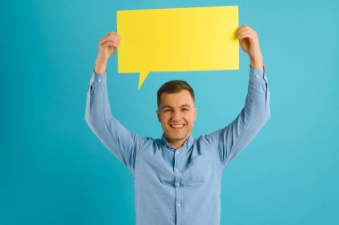 Neşeli Kafkasyalı adam mavi stüdyo arka planında boş plaket sergiliyor, tasarım için model.