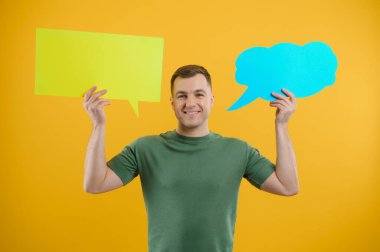 Neşeli genç erkek boş bir konuşma baloncuğu tutuyor ve parlak sarı arka plana karşı boş bir alan yaratıyor.