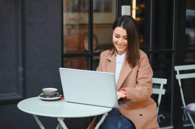 Laptopta çalışan, kafede oturup kahve içen çekici bir kadının fotoğrafı.