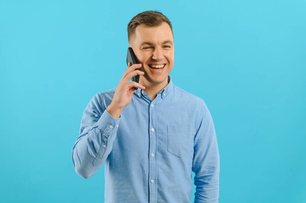 Young man in bright colorful wear talking on mobile cell phone on blue background. Trendy guy have conversation. Smartphone, technology concept.
