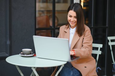 Caddedeki kafede dizüstü bilgisayarda çalışan mutlu bir kadın.
