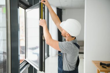 Yakışıklı genç adam yeni ev şantiyesine pencere takıyor.