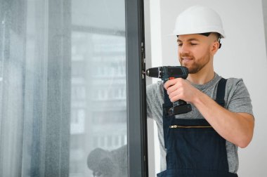 Yakışıklı genç adam yeni ev şantiyesine pencere takıyor.