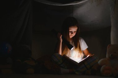 kitap ve el feneri ve oyuncak ayı çadırda okuma kız çocuk. yatmadan önce