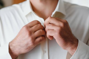 Bir adam düğmeleri gömleğinde takılır..