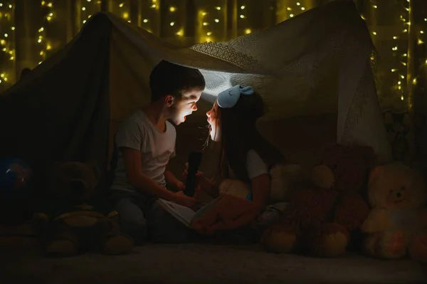 2人の小さな子供の家で夜には懐中電灯で本を読むためのキャンプテントを構築し 内部の睡眠を再生します ゲーム 創造性 アラームシステム — ストック写真