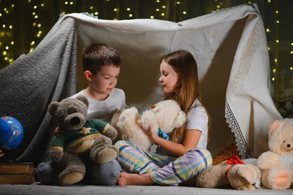 两个小孩晚上在家里玩耍 搭建起一个露营帐篷 用手电筒看书 然后睡在里面 警报系统的概念 — 图库照片