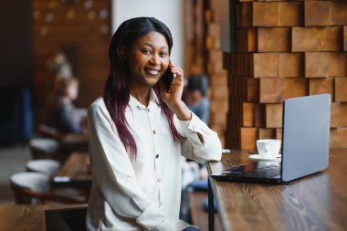 Genç iş kadını, bir sonraki iş toplantısını modern bir çalışma alanında dizüstü bilgisayar kullanarak ayarlıyor. Genç serbest çalışan kadın cep telefonundan e-posta ve diğer mesajları okuyor..