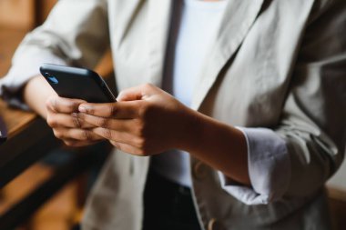 Afrika kökenli Amerikalı bir kadın cep telefonu mesajını internette tutuyor. Etnik melez kadınlar akıllı telefon tarayıcıları, kablosuz internet kullanırlar. Teknoloji, iletişim konsepti.