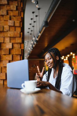 Kafede dizüstü bilgisayarla oturan gülümseyen Afro-Amerikan bir kadının portresi.