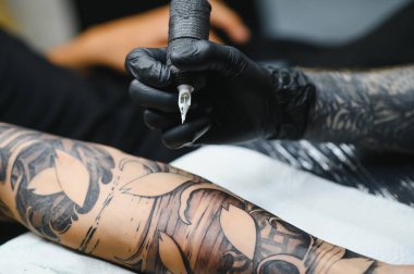 Dövme salonu. Dövme ustası bir adama dövme yaptırıyor. Dövme makinesi, güvenlik ve hijyen. Yakın plan, renkli, dövmeci..