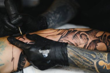 Dövme salonu. Dövme ustası bir adama dövme yaptırıyor. Dövme makinesi, güvenlik ve hijyen. Yakın plan, renkli, dövmeci..