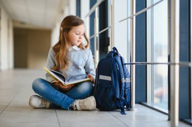 Kız gülümsüyor. Pencere ve okuma kitabı yakın otururken gülümseyen güzel liseli