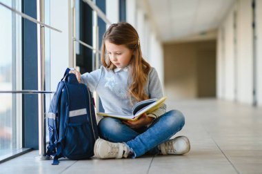 Okulun koridorları arasında el ele tutuşan küçük, güzel bir okul kızının ön görüntüsü. Komik ve mutlu kız kameraya gülümsüyor, ilkokul derslerinden sonra dinleniyor..