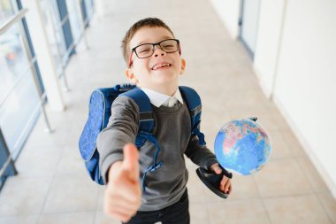 Gözlüklü mutlu çocuk ilk kez okula gidiyor. Elinde okul çantası ve kitabı olan bir çocuk. Çocuk sınıf odasının içinde. Okula geri dön..