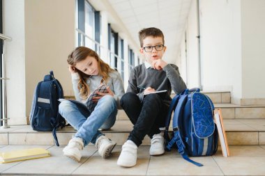 Okul koridorunda elinde kitaplarla gülümseyen çocukların portresi..