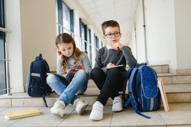 Okul koridorunda elinde kitaplarla gülümseyen çocukların portresi..