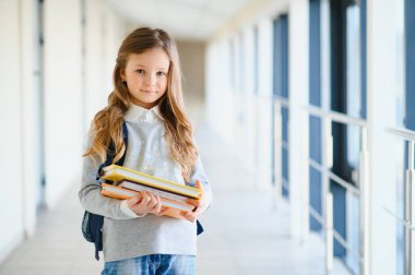 Okulun koridorları arasında el ele tutuşan küçük, güzel bir okul kızının ön görüntüsü. Komik ve mutlu kız kameraya gülümsüyor, ilkokul derslerinden sonra dinleniyor..