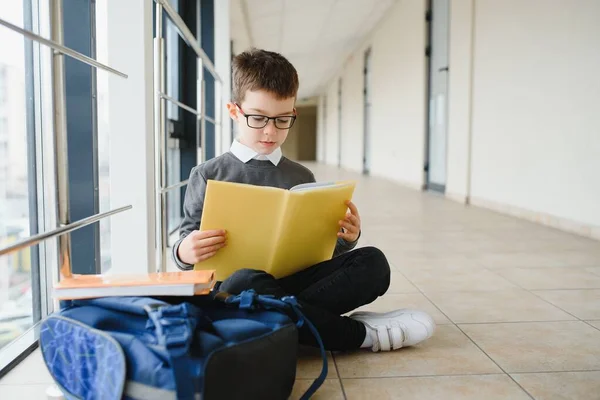 schoolboy sits on the floor of a school hallway and reads a book