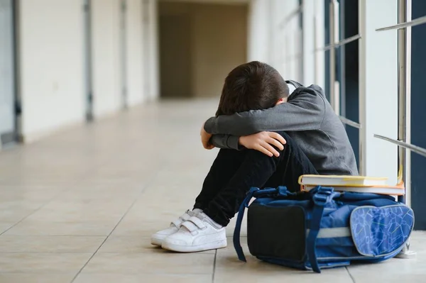 Sınıf arkadaşlarının zorbalığından sonra okulda oturup ağlayan üzgün bir çocuk. Çocuk elleriyle yüzünü kapattı ve ağladı..