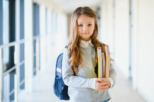 学校の廊下の間で小さな美しい学校の女の子のフロントビューでは 手でノートを保持します 面白いと幸せな女の子はカメラで笑顔 小学校でのレッスンの後に休憩 — ストック写真