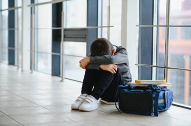 Yalnız çocuk arka planda iken zorbalık bir hareket acı sonra katta oturan çocuk. Koridorda ile oturan üzgün genç okullu çocuk bacaklarının arasında diz ve baş eller.
