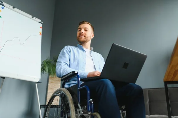 Disabled person in the wheelchair works in the office at the computer. He is smiling and passionate about the workflow.