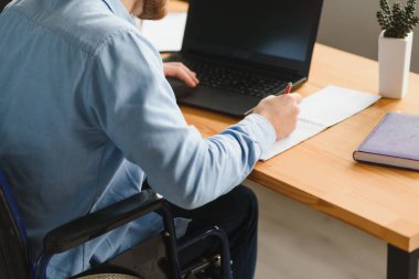 Tekerlekli sandalyede oturan ve ofiste bilgisayar kullanan engelli iş adamı.