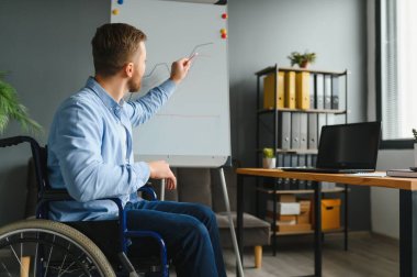 Tekerlekli sandalyede oturan ve ofiste bilgisayar kullanan engelli iş adamı.