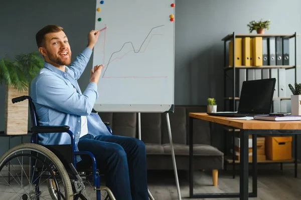 Handicapped Businessman Sitting On Wheelchair And Using Computer In Office