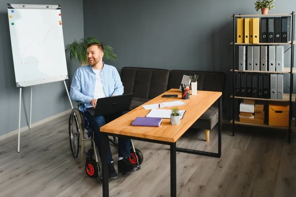 Young happy entrepreneur in wheelchair working on laptop at home.