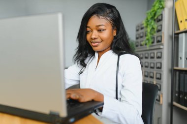 Hastane ofisinde steteskoplu beyaz önlüklü gülümseyen kadın doktor portresi.