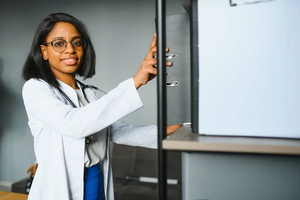 Smiling young adult indian female doctor wear white coat in medical clinic office. Happy beautiful health care india professional medic physician, therapist, headshot portrait.